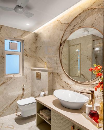 Marble-clad bathroom with round brass mirror, floating vanity, and wall-hung toilet