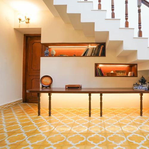 Foyer under a staircase with patterned yellow tile floor, wooden console, and lit display niches