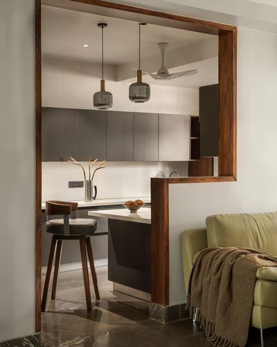 Kitchen framed by a thick wood portal, with pendant lights over a stone-topped island and green sofa in foreground
