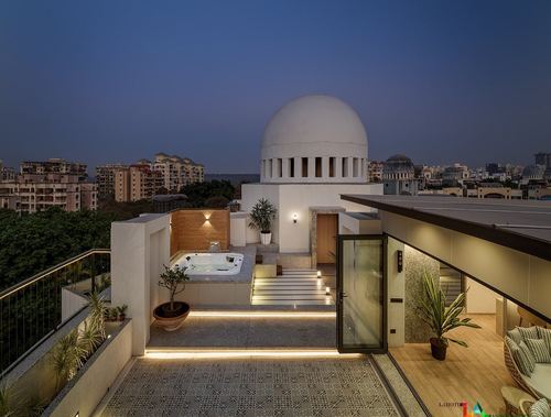 Rooftop terrace at dusk with jacuzzi, illuminated steps, and a domed white structure against city skyline