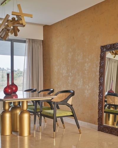 Dining area with cane-back chairs, brass-legged marble table, and ornate mirror against ochre wall