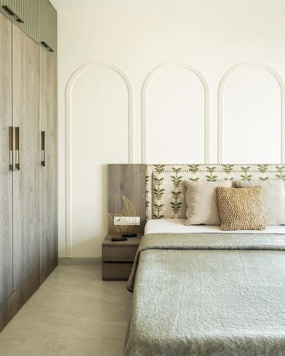 Bedroom with arched wall panelling, wood wardrobe, and floral upholstered headboard in neutral tones