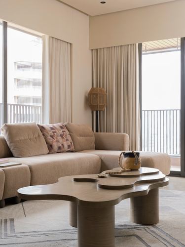 Beige living room with curved sectional sofa and organic wood coffee table facing floor-to-ceiling windows