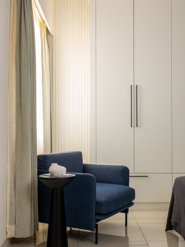 Navy blue armchair beside black pedestal table against cream wardrobe wall with sheer curtains