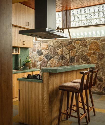Kitchen with fluted wood cabinetry, green stone counters, and a rugged stone accent wall