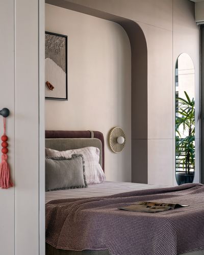 Bedroom seen through open door, upholstered headboard under curved plaster archway, mirror and plant beyond
