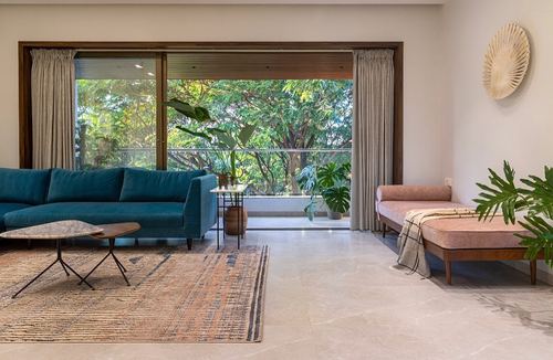 Living room with teal sofa and pink daybed facing a glazed wall overlooking green trees