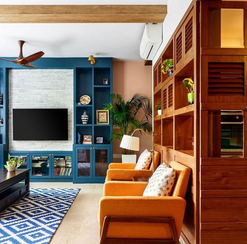 Living room with teal built-in shelving, stone TV wall, orange armchairs and wood partition