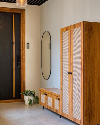 Foyer with black door, oval mirror, and tall cane-paneled wooden wardrobe beside matching console