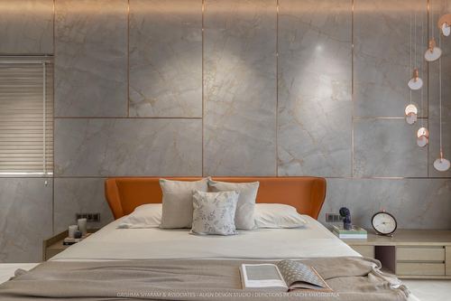 Bedroom with orange leather headboard against marble-panelled wall and hanging circular pendant lights