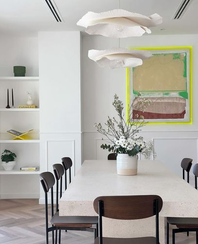White dining room with terrazzo table, dark wood chairs, sculptural pendant lights, and colorful abstract art