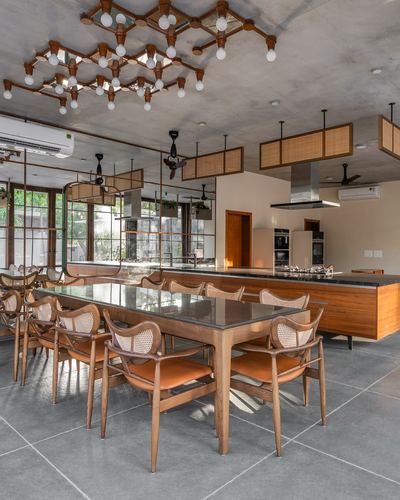 Open dining and kitchen area with cane chairs, wood table, and cluster pendant lighting under exposed concrete ceiling