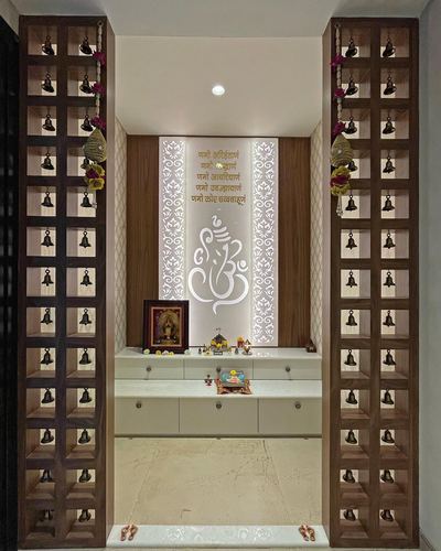 Symmetrical pooja alcove with jali pillars hung with bells, backlit Ganesha motif panel, and marble floor