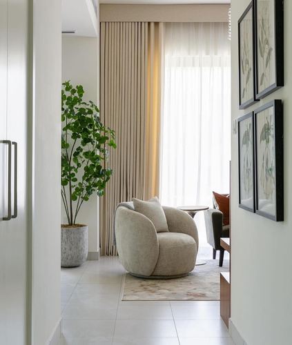 Hallway view into a living room with a round cream armchair, potted plant, and framed prints
