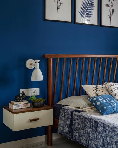 Blue bedroom wall with wood spindle headboard, white sconce, and floating nightstand with books and figurine