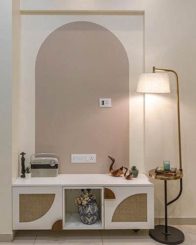 Arched mauve niche above cane-front console with brass floor lamp beside it