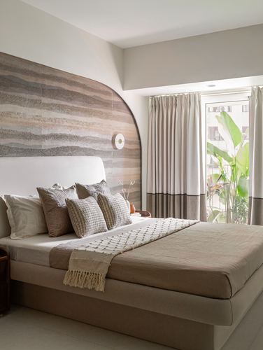 Neutral-toned bedroom with arched textured stone wall behind upholstered bed and balcony view