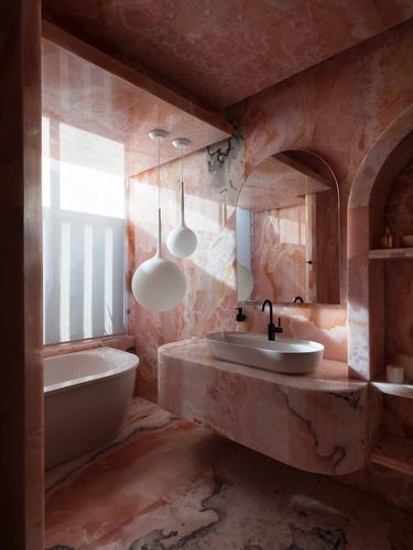 Bathroom fully clad in pink veined stone with oval tub, globe pendants, and arched mirror