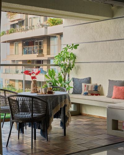 Balcony with round table, cane chairs, potted plants, and a built-in stone bench with cushions overlooking the city