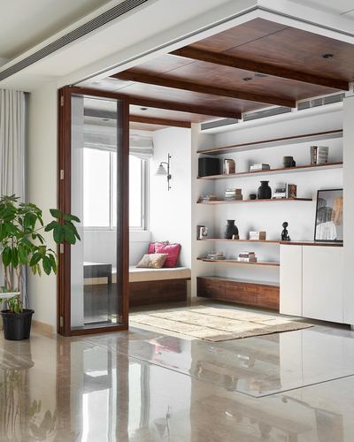 Living room nook with wood ceiling, window seat, open shelving and folding glass doors over polished stone floor