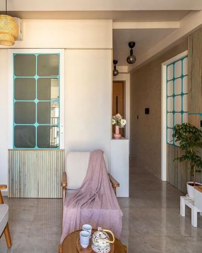 Living room corner with teal-framed glass partition, wooden armchair draped in pink throw, and view into hallway