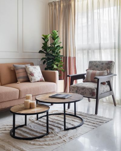 Living room with blush sofa, floral armchair, and nesting cane coffee tables near sheer curtained window