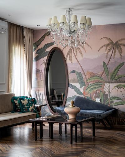 Living room with tropical mural wall, oval mirror, crystal chandelier, and blue velvet sofa