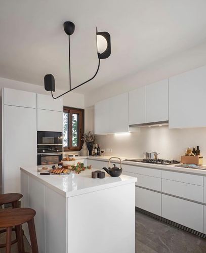 All-white kitchen with island counter and sculptural black pendant light fixture