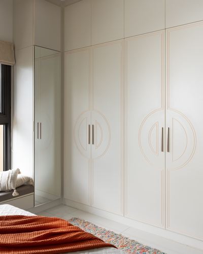 White art deco wardrobe with circular handle motifs beside a mirrored door and window seat