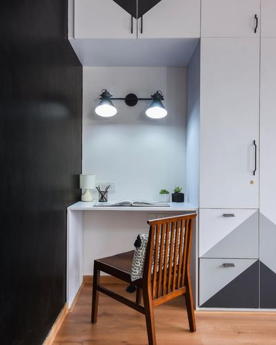 Small white study nook with black wall, twin wall sconce, and wooden chair against patterned wardrobe