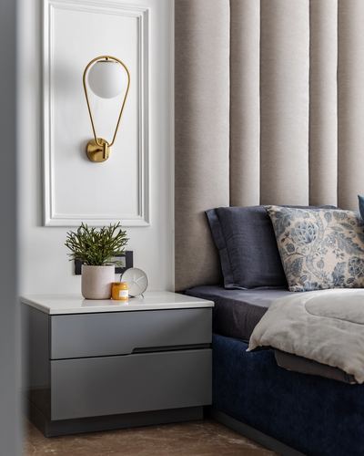 Bedroom nightstand with brass sconce beside a channel-tufted navy velvet bed