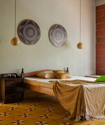 Kerala-style bedroom with wooden bed, mustard bedding, patterned tile floor and rattan pendant lights