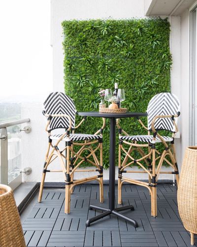 Balcony bistro set with chevron rattan chairs against a green wall backdrop