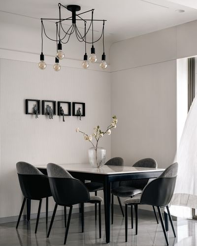 Monochrome dining room with black chairs, marble-top table, and cascading bulb chandelier