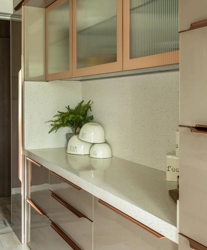 Cream terrazzo kitchen counter with rose gold handles and fluted glass cabinets, small plant and bowls