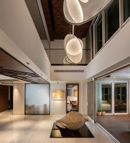 Double-height foyer with large disc pendant lights, marble floor, wood-slat ceiling and glimpse of living room beyond
