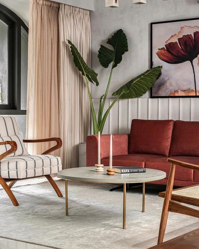 Living room with rust sofa, striped armchair, round stone coffee table and large leafy plant