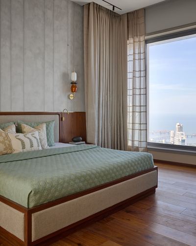 Bedroom with sage green bedding, wood-panelled wall, and floor-to-ceiling window overlooking Mumbai coastline