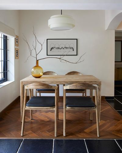 Wooden dining table with leather-seat chairs on herringbone floor beneath a drum pendant light