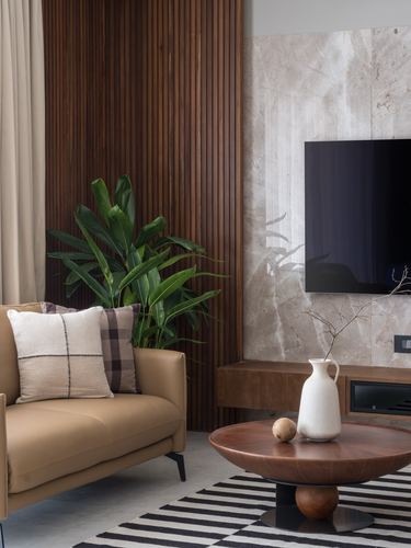 Living room corner with tan sofa, wood-slat wall, marble tv wall and round wood coffee table