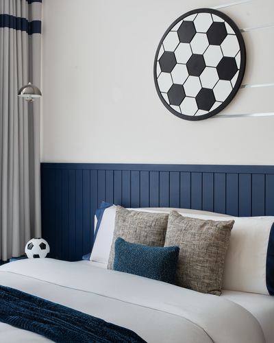 Kids bedroom with navy wainscot headboard wall, round soccer-ball wall art, and layered pillows
