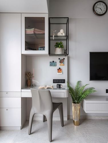 Small built-in study desk with grey chair, glass cabinet above, and fern planter beside a TV console.
