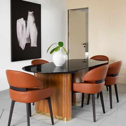 Dining room with oval stone-top table on curved wood base surrounded by orange leather chairs