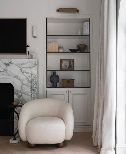 Cream boucle armchair beside a green marble fireplace and black-framed bookshelf