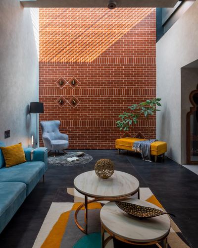 Living room with exposed brick wall, teal sofa, mustard bench, and round marble nesting tables