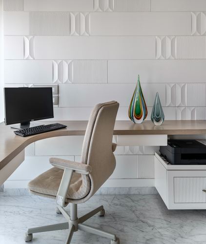 Home office desk with monitor, cream chair, and glass decor against textured white wall