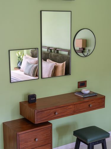 Green bedroom wall with mirrors reflecting a sofa, above a floating wood console and drawers