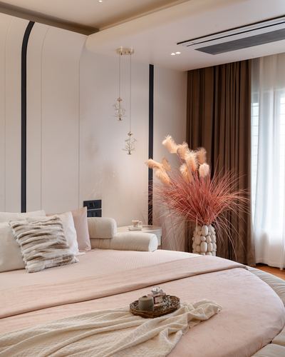 Curved blush-pink bed in a softly lit bedroom with pampas grass and hanging pendant lights