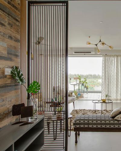 Living room with vertical metal slat screen dividing space, weathered wood wall, and balcony view beyond
