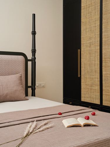 Bedroom corner with black four-poster bed, rose linens, and cane-paneled wardrobe with brass handles